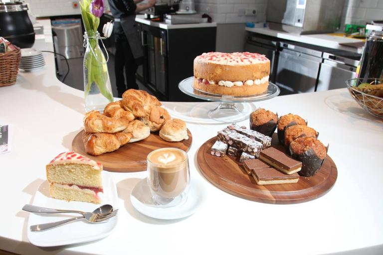 A white table showing an array of cakes and a flat white coffee.