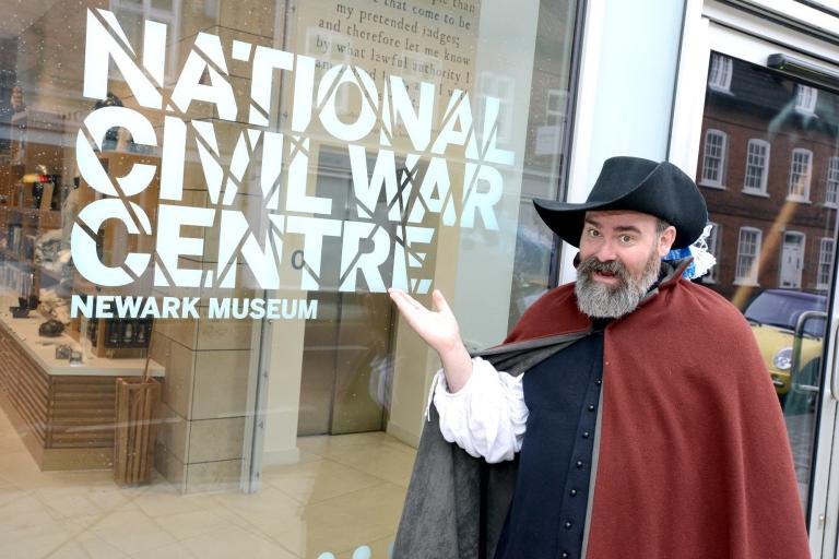 A man in a red cape and black hat poses outside of the National Civil War Centre entrance.