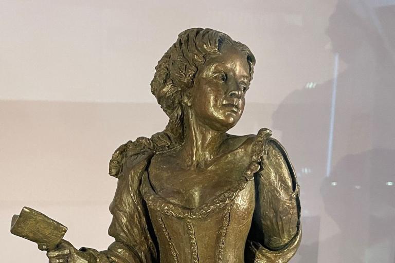 A gold statue of a lady in a dress carrying a small book.
