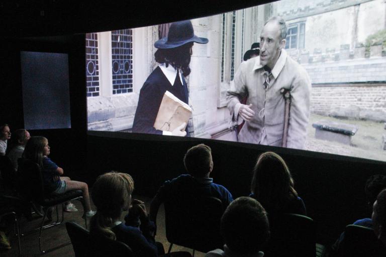 A group of people watching a large screen showing an historical event.