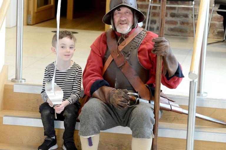 A man dressed in historical military-style clothing sits with a boy on a the steps of National Civil War Centre.