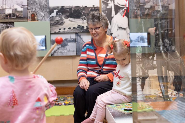 A woman and two young children playing in a gallery space 