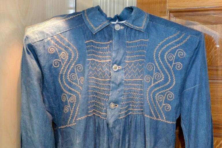 An historial piece of blue clothing with a yellow stitched pattern with three white buttons..