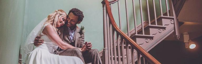 A married couple on their wedding day sat on a staircase 