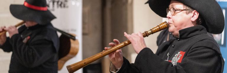 Two men dressed up in black costumes wearing hats playing musical instruments