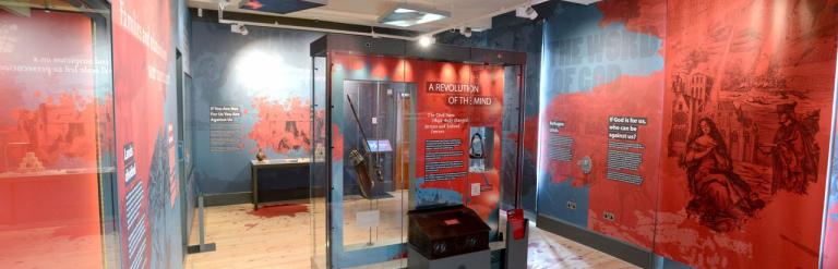 A gallery room showing red and black wallpaper that depicts information on historial conflict and creativity.